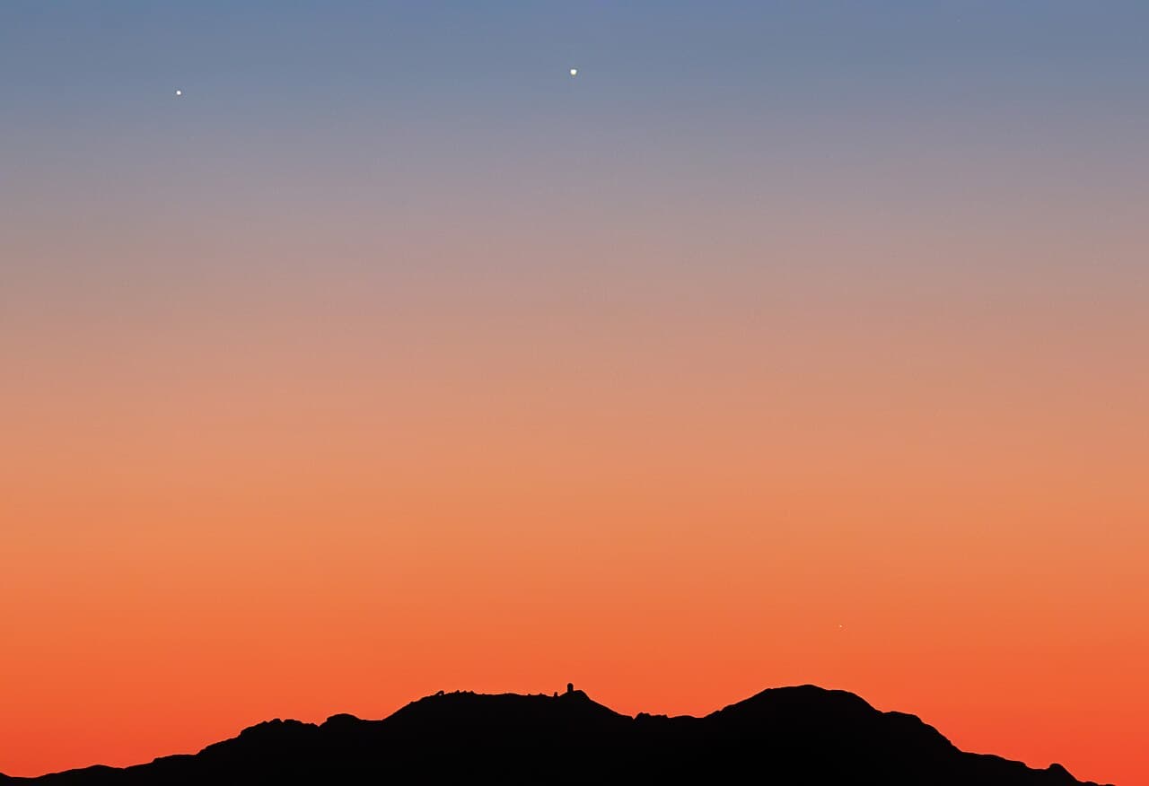 Conjonction planétaire au crépuscule au-dessus d'une chaîne de montagnes, deux astres brillants visibles dans le ciel orangé
