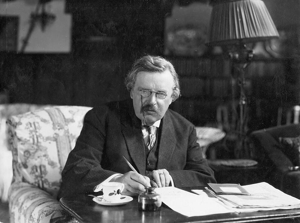 G. K. Chesterton seated at his desk, pen in hand.
