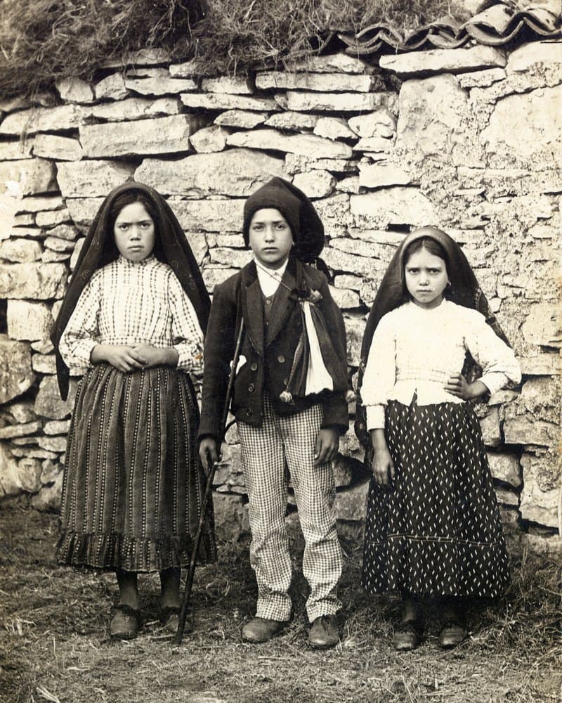 Lúcia, Francisco et Jacinta debout devant un mur de pierres sèches