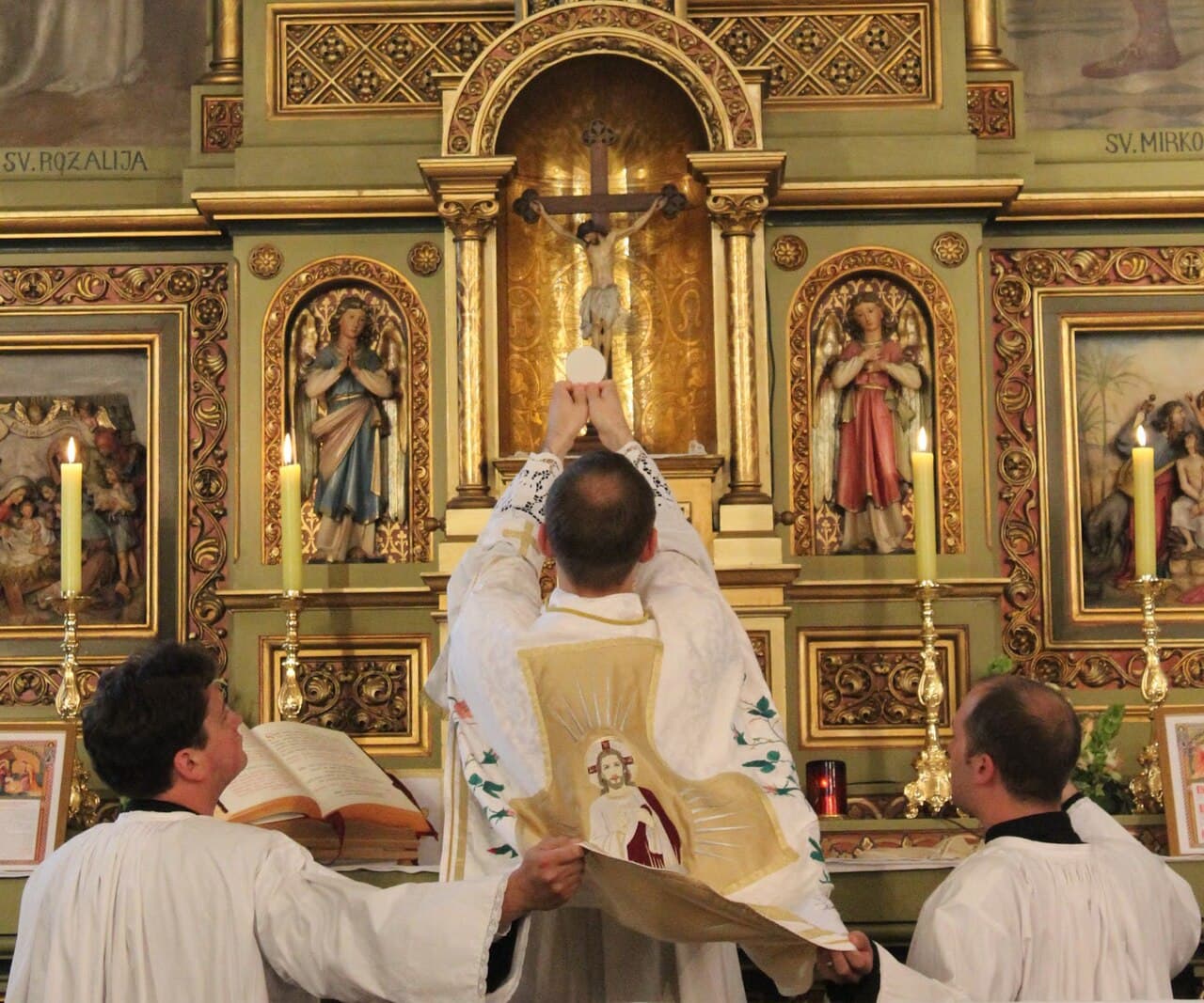 Ein Priester erhebt die konsekrierte Hostie während der Messe vor dem Altarkruzifix.