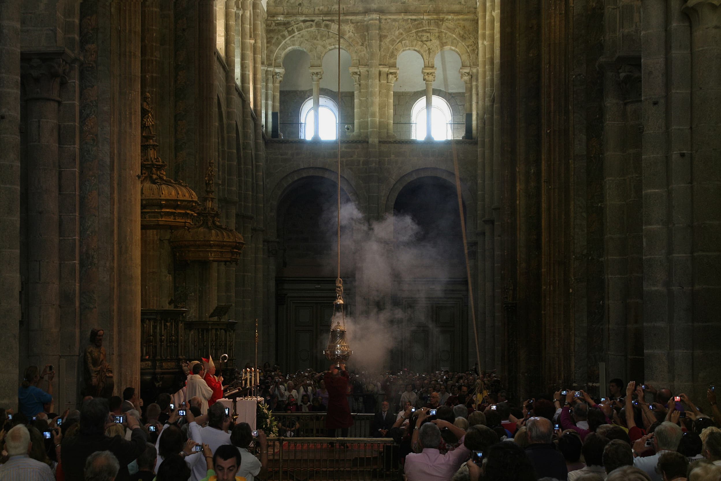 O Botafumeiro a atravessar o transepto da catedral de Santiago entre fumo de incenso, sobre a multidão