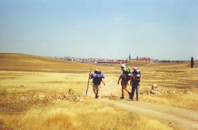 Peregrinos com mochilas num caminho rural para Salamanca, com seta amarela