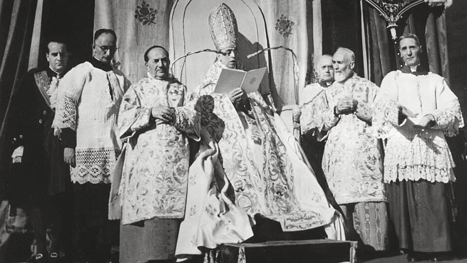 Pio XII proclamando o dogma da Assunção desde a loggia da basílica de São Pedro, em 1.º de novembro de 1950, rodeado de prelados.