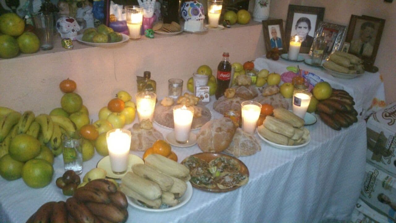 Meyveler, ekmekler, mumlar ve fotoğraflarla donatılmış Meksika aile sunağı.